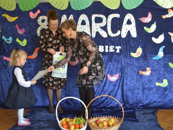 Zdjęcie przedstawia moment wręczenia dyplomu i nagrody dla dziewczynki w konkursie plastycznym przez panią Dyrektor i panią prowadzącą. 