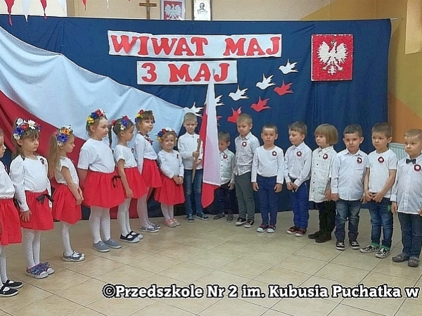 Dzieci ustawione są w półkolu w tle patriotycznej dekoracji