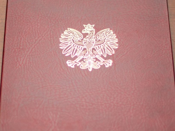 bordowa teczka ze złotym orłem, z prawj strony leży czarne pióro