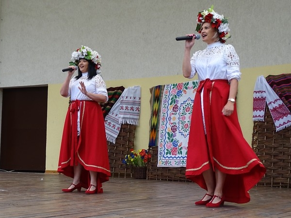 Na scenie stoją trzy kobiety w czerwonych długich spudnicach. Na głowach miają wiadnki.