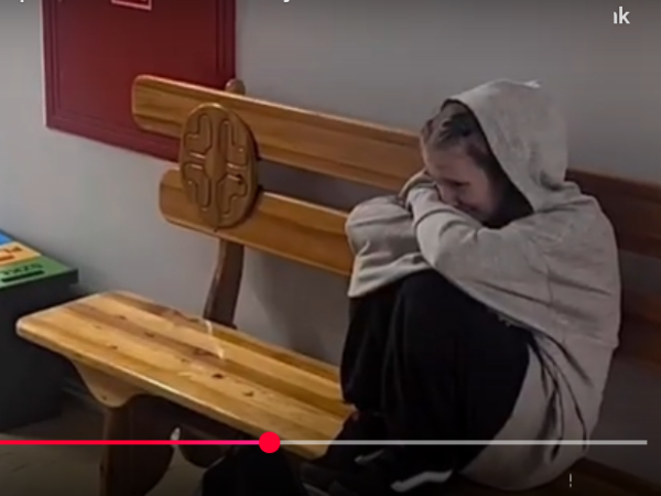na ławce siedzi dziewczyna z podkulonymi nogami. Płacze