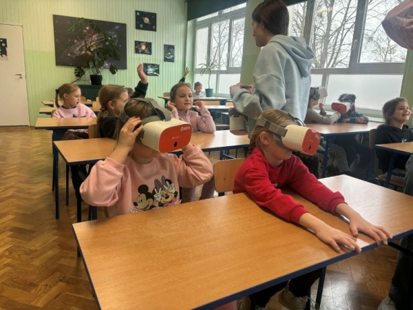 Dzieci siedzą w ławkach, mają na sobie okulary wirtualnej rzeczywistości.