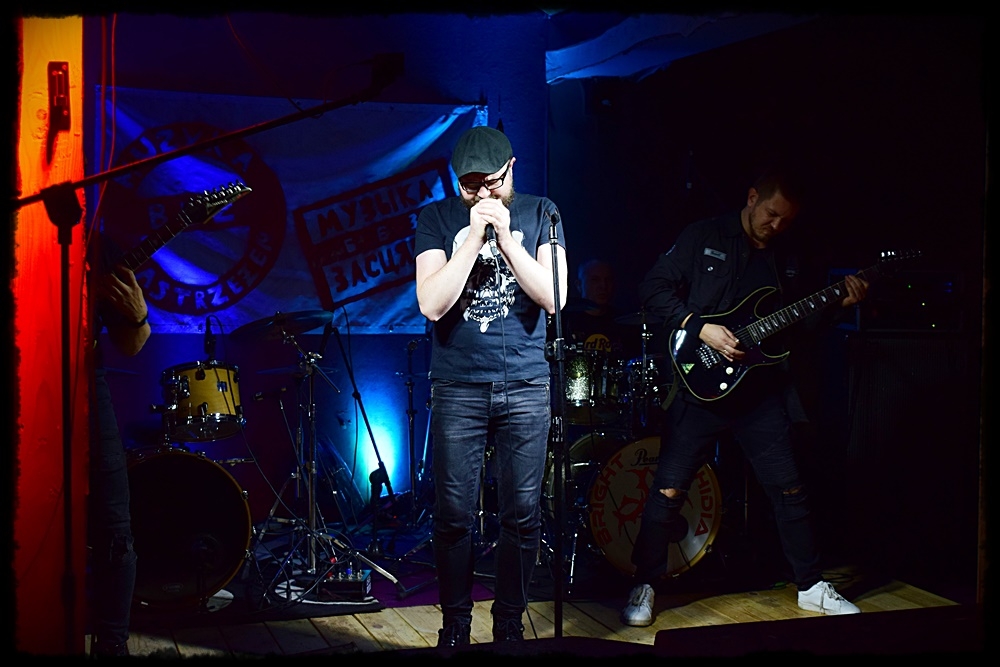 mężczyzna przy mikrofonie za nim grupa muzyków