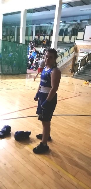 Zawodnik ubrany w niebieski strój bokserski troi na boisku, przed nim leżą rękawice bokserskie.