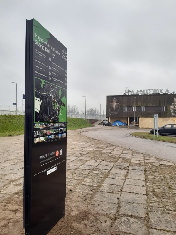 tablica turystyczna, w oddali widnieje budynek dawnego hajnowskiego dworca