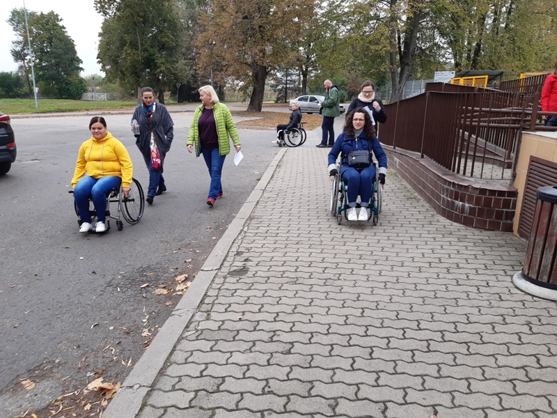 uczestnicy szkolenia podczas spaceru - część z nich jest na wózkach inwalidzkich, a przy nich asystenci