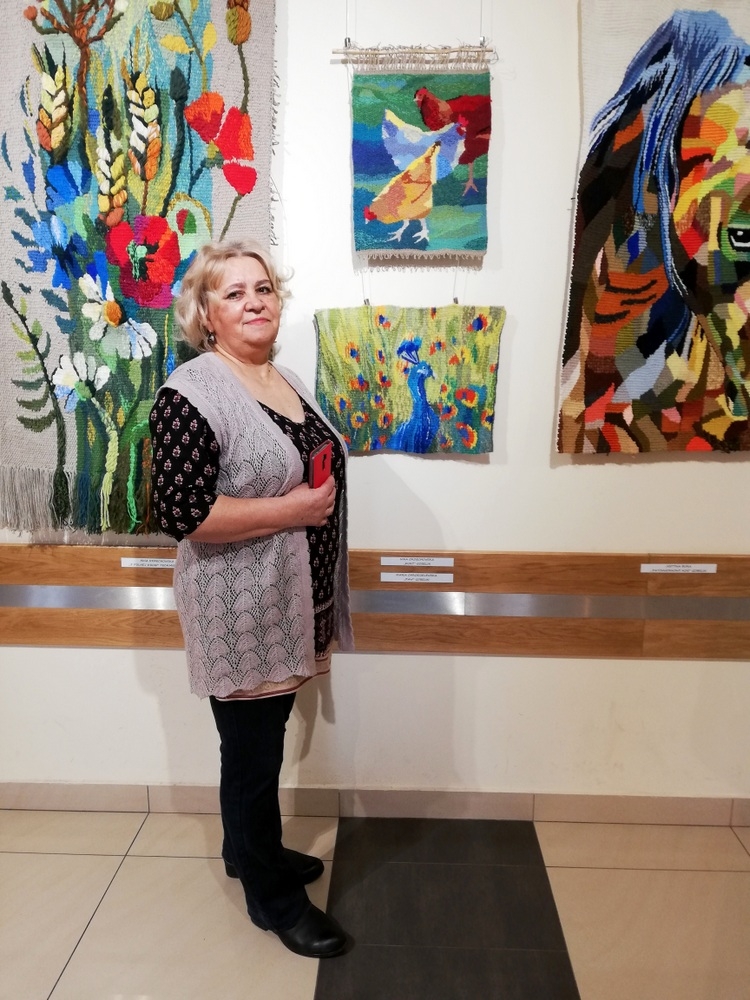 Zdjęcie przedstawia uczestników Pracowni Gobelinu oraz ich prace podczas wernisażu wystawy gobelinów pt. „W moim ogrodzie”
