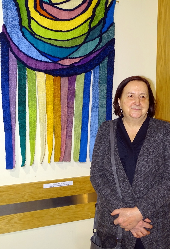 Zdjęcie przedstawia uczestników Pracowni Gobelinu oraz ich prace podczas wernisażu wystawy gobelinów pt. „W moim ogrodzie”