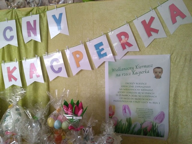 Na pierwszym zdjęciu widać plakat informujący o Kiermaszu Wielkanocnym na rzecz Kacpra Smyka o treści: „Drodzy rodzice serdecznie zapraszamy na Wielkanocny Kiermasz, który odbędzie się w dniach 22-23 marca w godzinach od 1400-1600 w holu Przedszkola nr 5 przy ulicy M. Reja 2. Pieniądze uzyskane ze sprzedaży ozdób zostaną przekazane na rzecz naszego wychowanka Kacpra Smyka”.