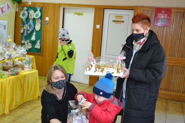 Na zdjęciu widać matkę z synem. Matka trzyma wybraną ozdobę a dziecko wrzuca pieniądze do skrzynki , którą trzyma jedna z organizatorek.