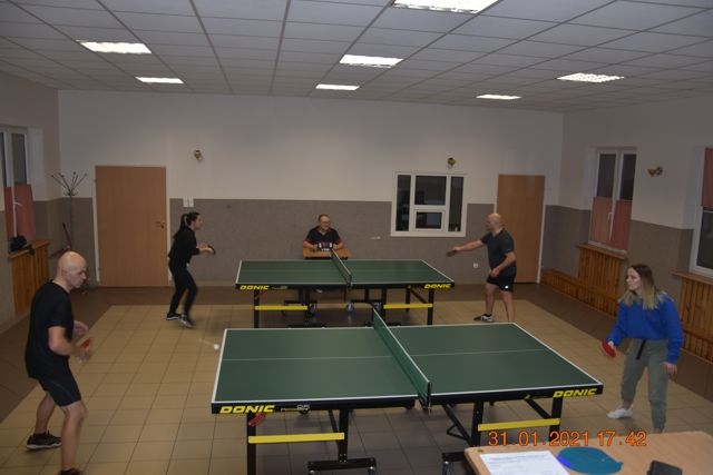 na srodku ssali stoją dwa stoły do tenisa. Po bokach rozgrywający zawodnicy.