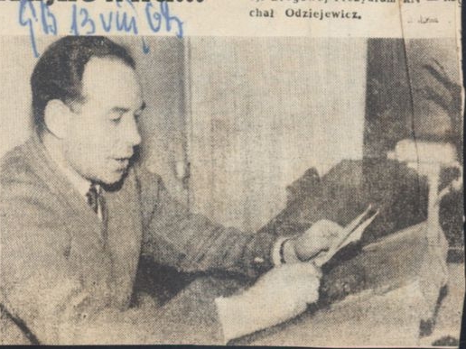 skan czarno-białego zdjęcia prasowego; na zdjęciu siedzący przed mikrofonem mężczyzna czyta coś z kartki