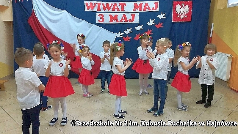 Wspólne grupowe zdjęcie dzieci z grupy III Puchatki przy fladze i napisie Wiwat 3 maj w którym chłopcy stoją z tyłu, a dziewczyny siedzą z przodu na krzesełkach.