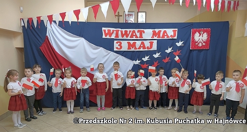 Dzieci z grupy II Kangurki ustawione w półkolu na zmianę chłopak - dziewczyna, gdzie niektóre dzieci trzymają flagę biało - czerwoną recytują wiersz "Barwy ojczyste".