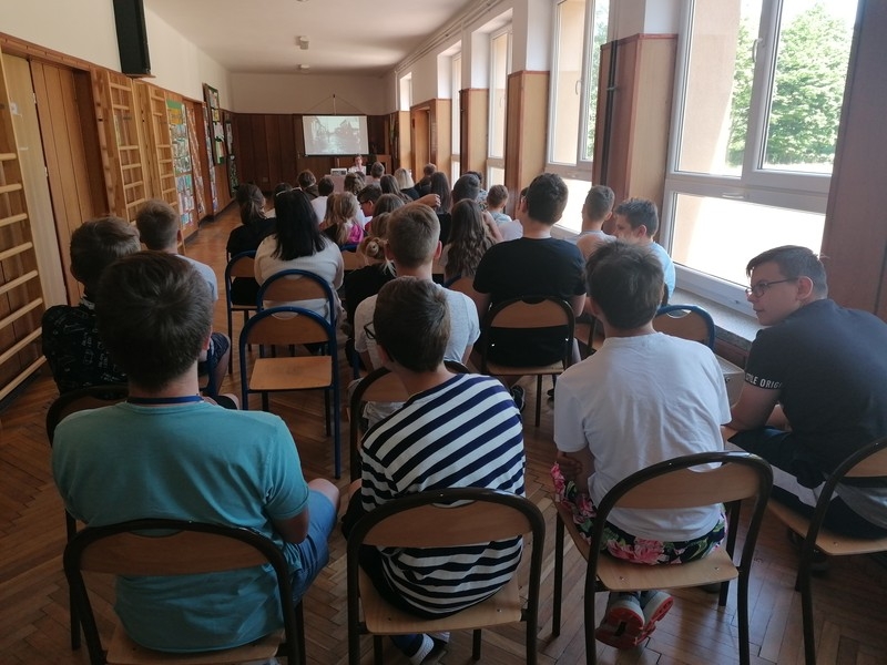 Zdjęcie uczniów i prowadzącej zrobione z końca sali.