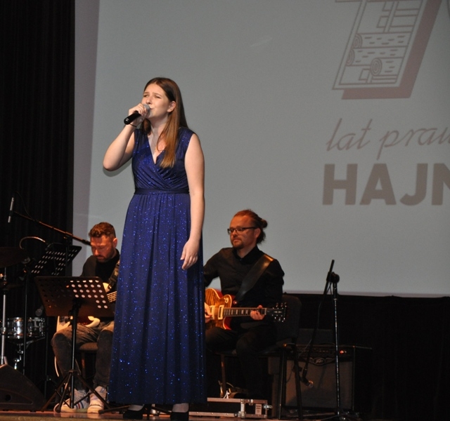 dziewczyna w długiej granatowej sukience na scenie, za nią muzycy