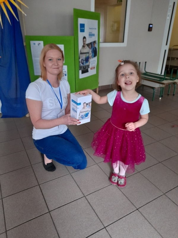 nauczycielka – wolontariuszka w towarzystwie dzieci, które wrzucają pieniądze do puszki.