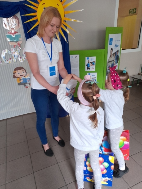 nauczycielka – wolontariuszka w towarzystwie dzieci, które wrzucają pieniądze do puszki.