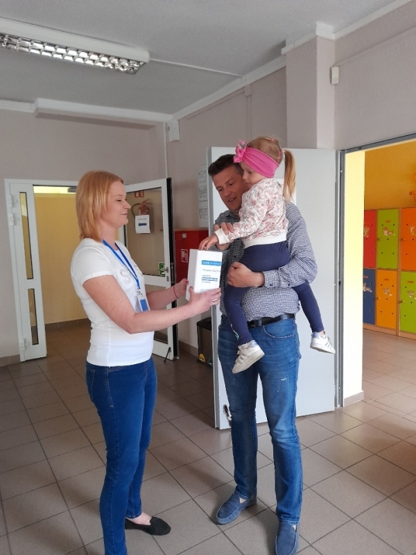 nauczycielka – wolontariuszka w towarzystwie dzieci, które wrzucają pieniądze do puszki.