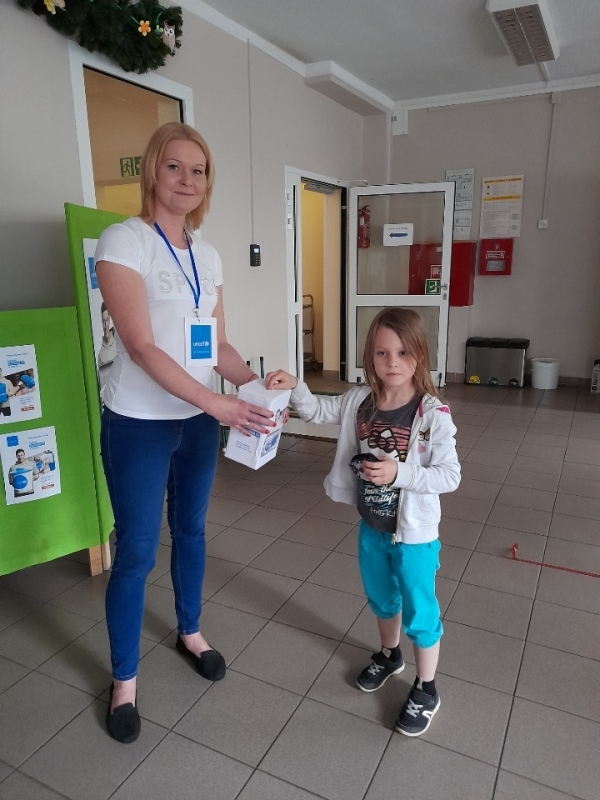 nauczycielka – wolontariuszka w towarzystwie dzieci, które wrzucają pieniądze do puszki.