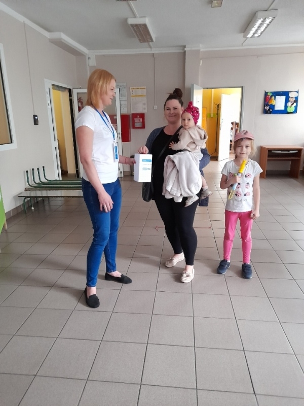 nauczycielka – wolontariuszka w towarzystwie dzieci, które wrzucają pieniądze do puszki.