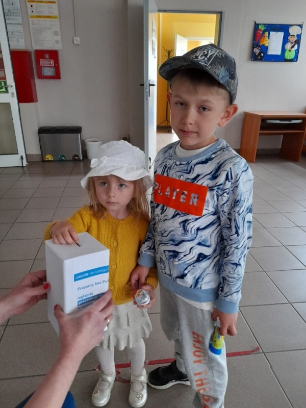dzieci na tle plakatu UNICEFU, każde z nich wrzuca do puszki pieniądze.