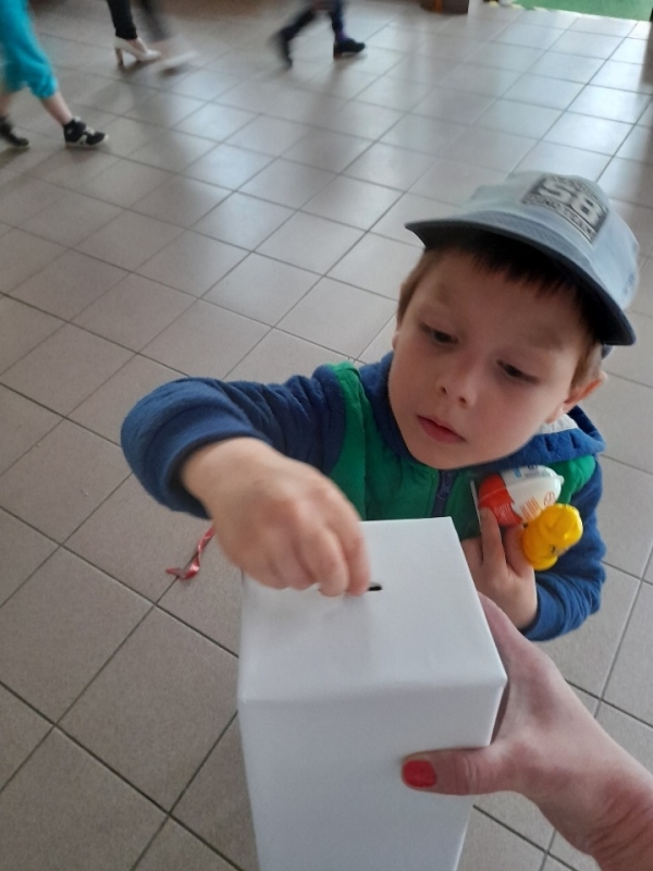 dzieci na tle plakatu UNICEFU, każde z nich wrzuca do puszki pieniądze.