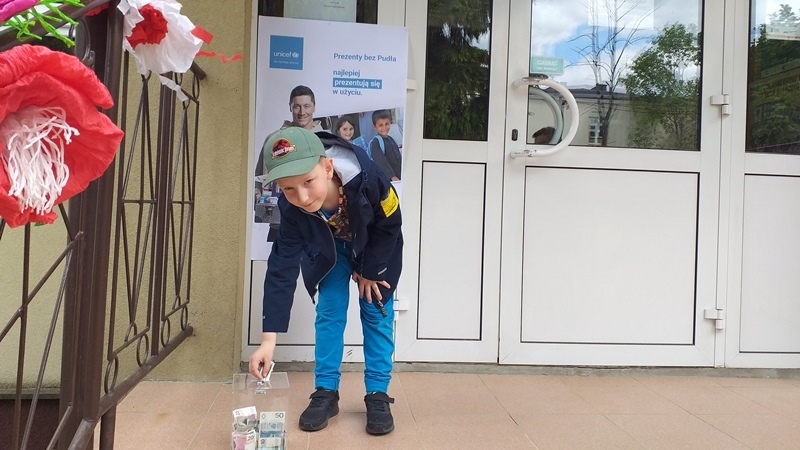 dzieci na tle plakatu UNICEFU, każde z nich wrzuca do puszki pieniądze.
