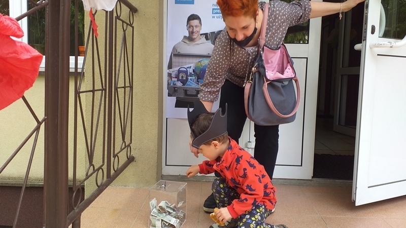 dzieci na tle plakatu UNICEFU, każde z nich wrzuca do puszki pieniądze.