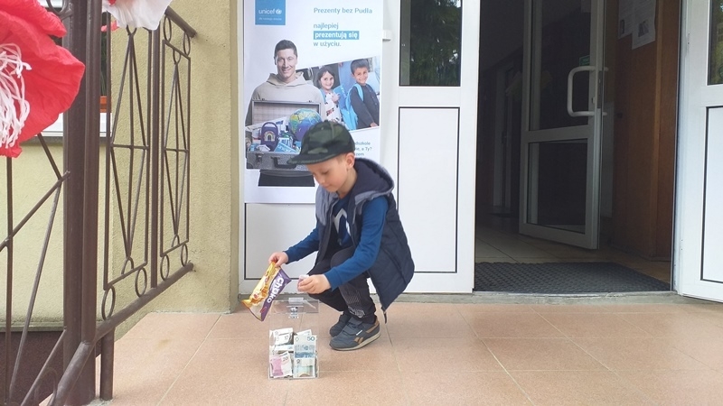 dzieci na tle plakatu UNICEFU, każde z nich wrzuca do puszki pieniądze.