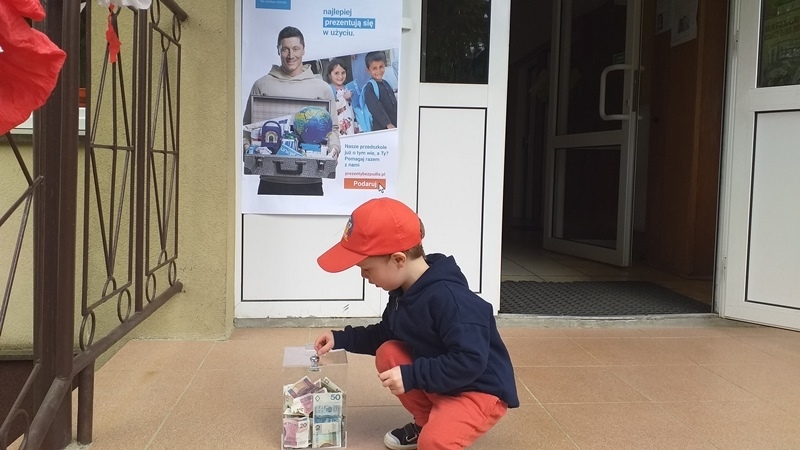 dzieci na tle plakatu UNICEFU, każde z nich wrzuca do puszki pieniądze.