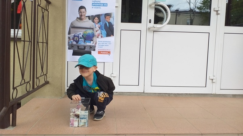 dzieci na tle plakatu UNICEFU, każde z nich wrzuca do puszki pieniądze.
