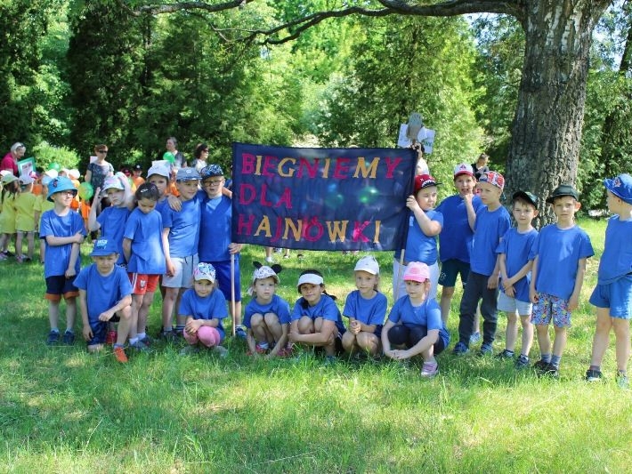 Przedszkolaki ubrane w jednakowe niebieskie koszulki trzymają plakat z napisem "Biegniemy dla Hajnówki"
