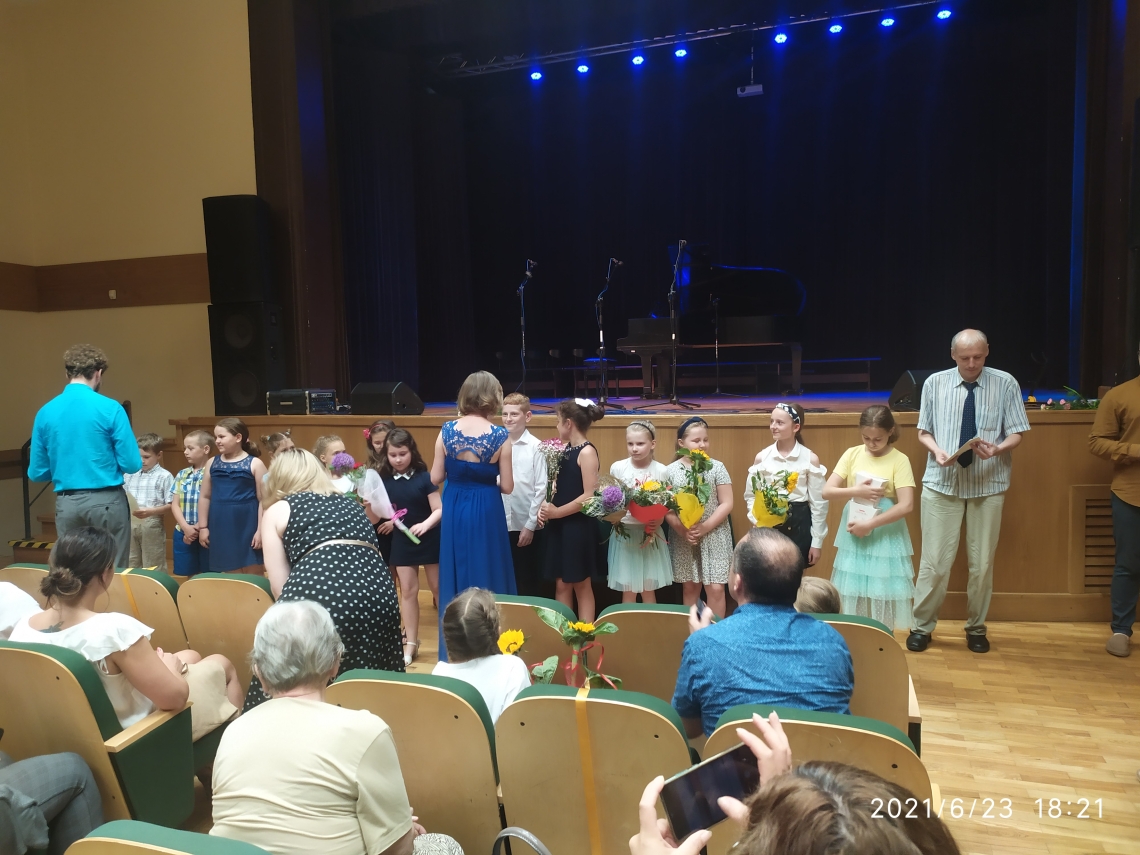 grupa uczniów ustawiona w szeregu, każdy z nich trzyma w ręku bukiet kwiatów