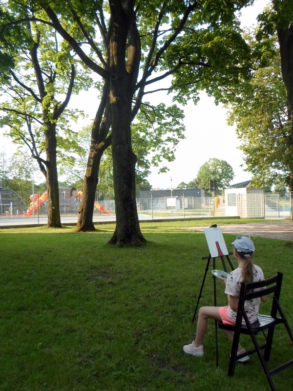 dziewczynka siedzi na krześle, przed nią stoi sztaluga z płótnem