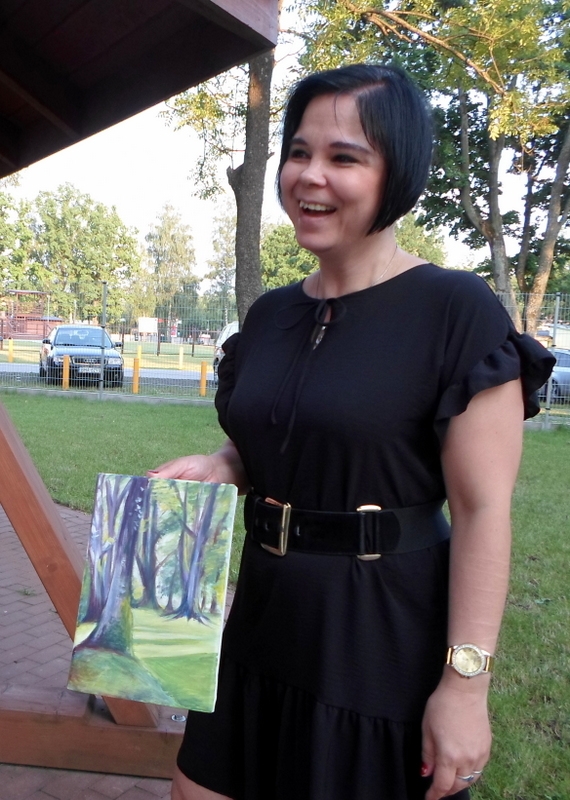 kobieta w czarnej sukience trzyma w ręku namalowany pejzaż