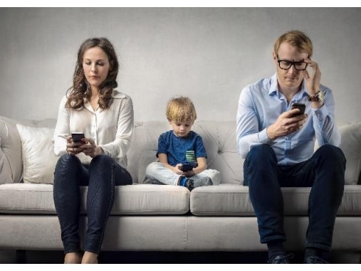 Dwie dorosłe osoby i jedno dziecko siedza na kanapie. Wszyscy trzymają w dłoniach telefony.