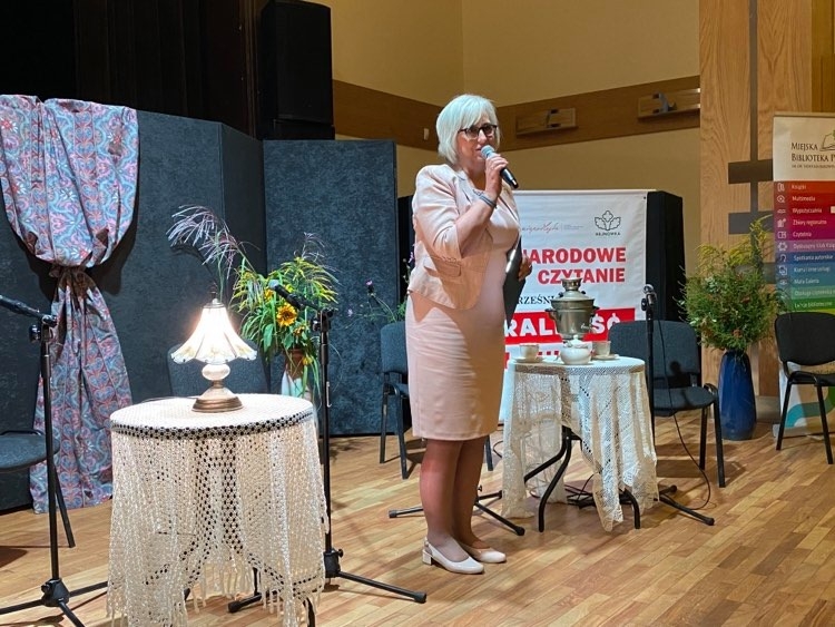 Na scenie stoi kobieta i mówi do mikrofonu