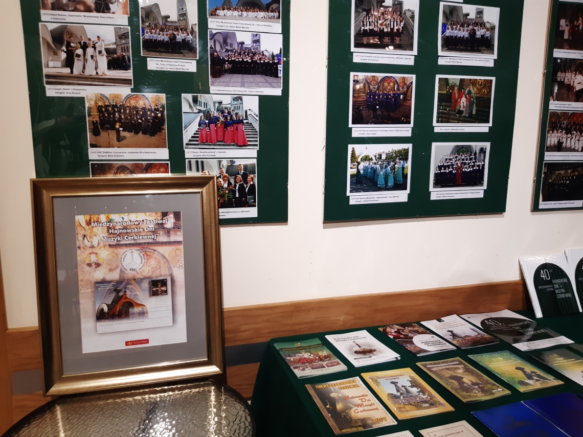 część wystawy, plansze ze zdjęciami, aarchiwalne foldery ułożone na stoliku, ramka z kartką pocztową