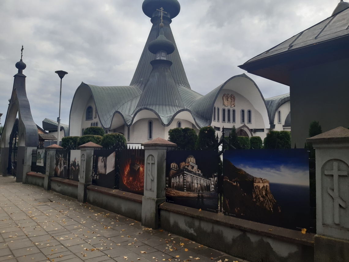 zawieszona wystawa zdjęć na ogrodzeniu soboru, w tle świątynia