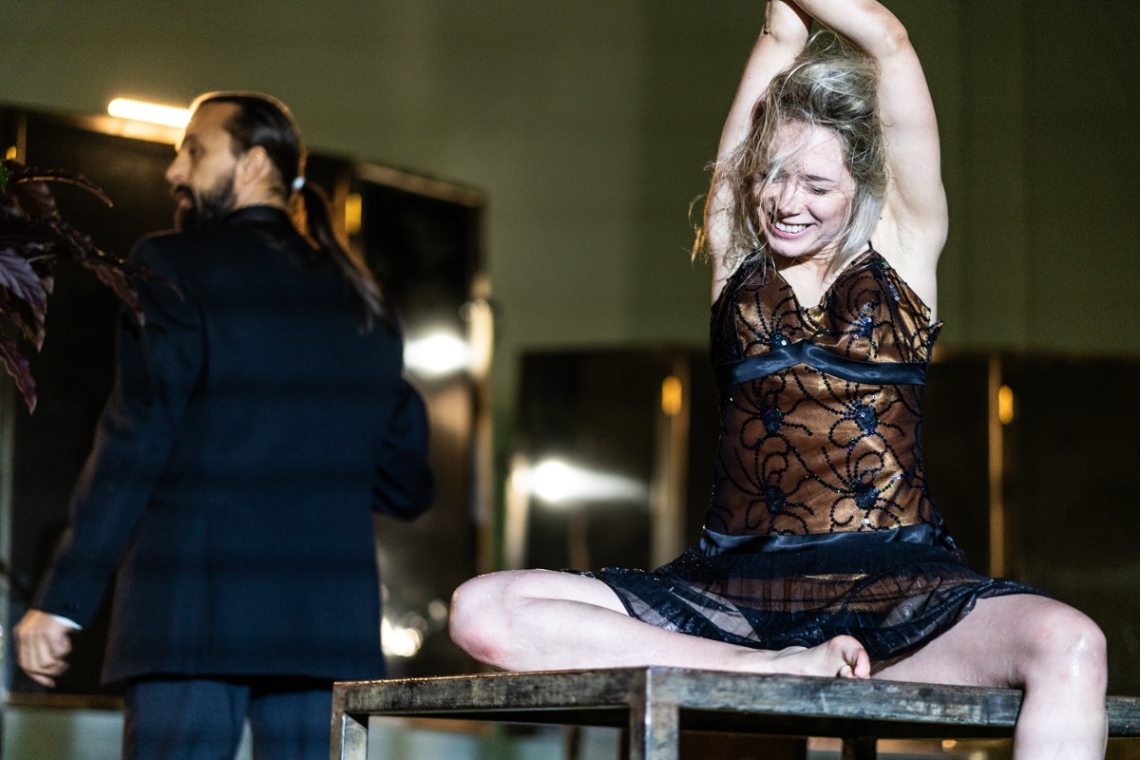 kobieta siedząca na stole z uniesionymi do góry rękoma, ubrana w czarną koronkową halkę