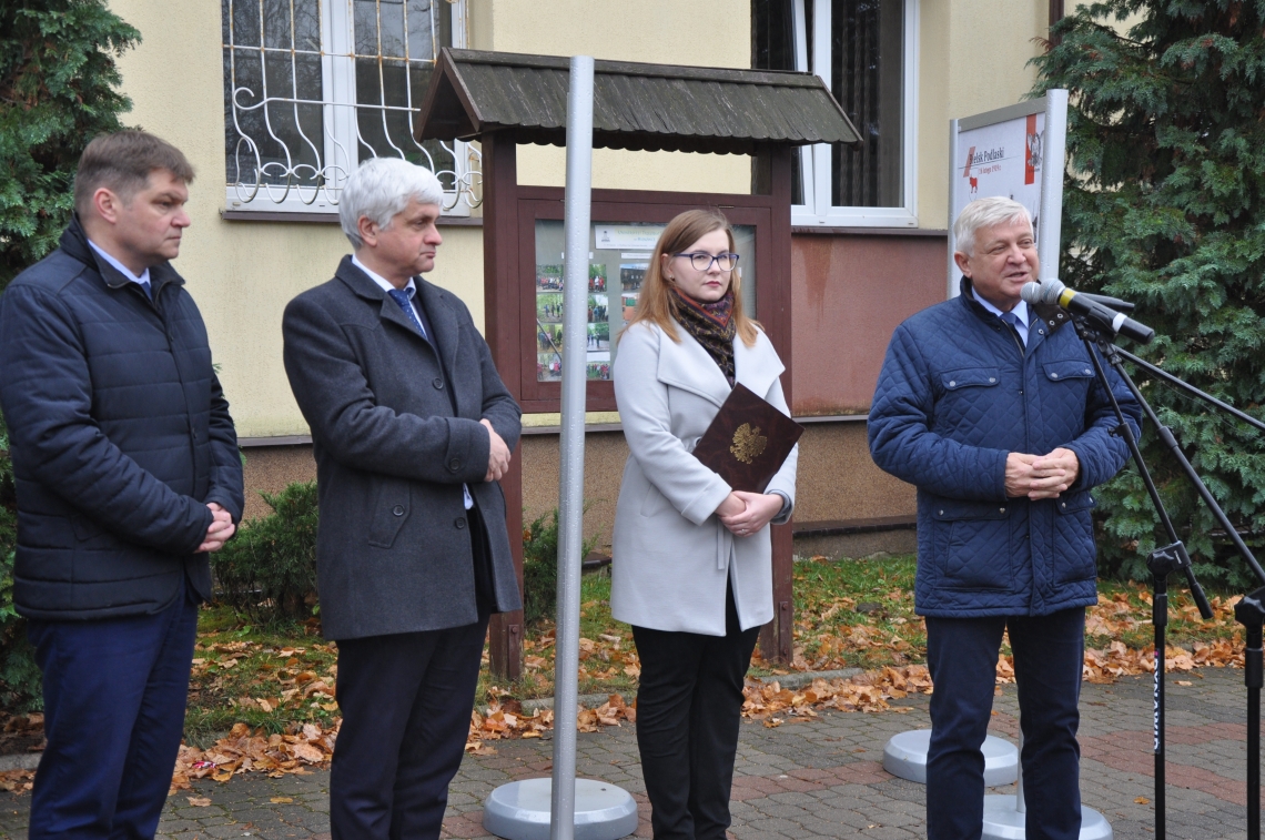 grupa osób stoi przy wystawie, jeden z mężczyzn wypowiada się do mikrofonu