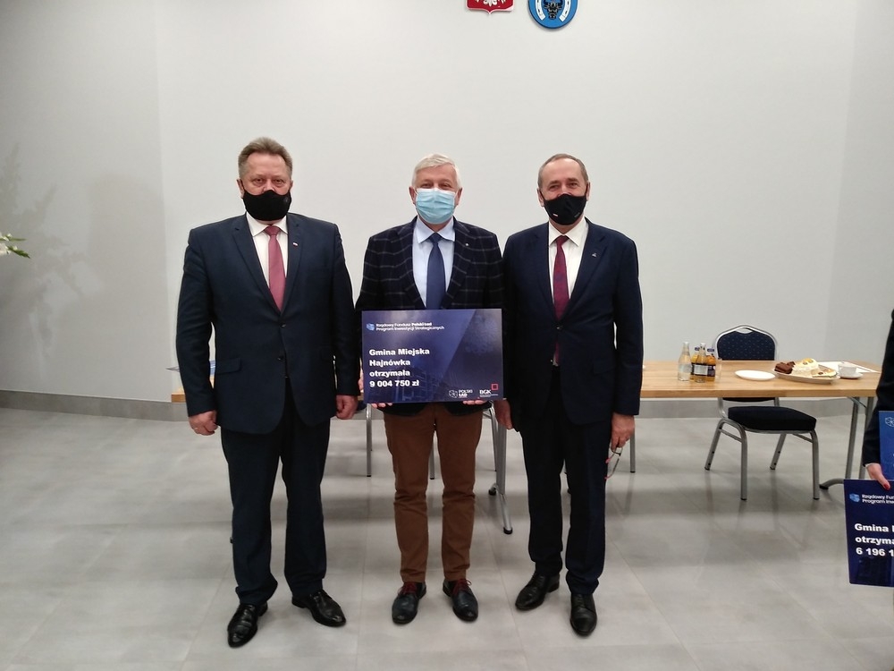 Zdjęcie pamiątkowe, na którym stoi trzech mężczyzn. Burmistrz trzyma symboliczny czek.