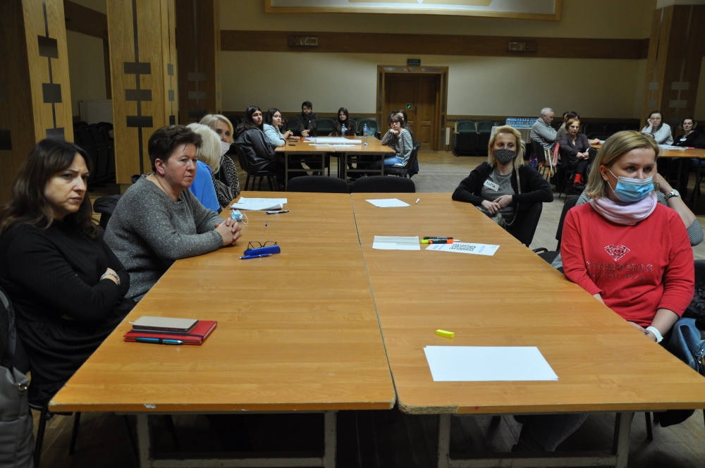 Uczestnicy siedzą przy stole, w głębi sali widać dwa stoły z uczestnikami spotkania