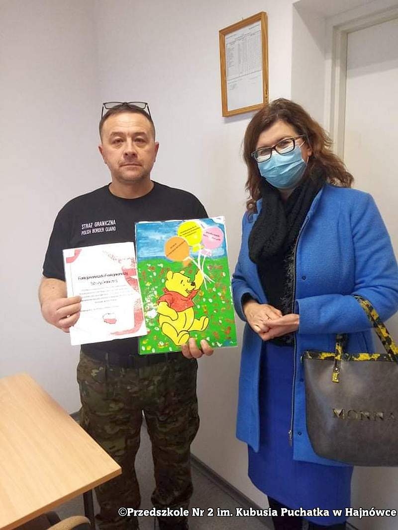 Zdjęcie kobiety i mężczyzny, stoją obok siebie a mężczyzna pokazuje otrzymane prace plastyczne.