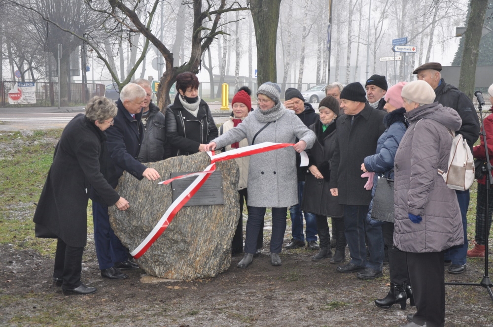 Zdjęcie grupowe, uczestnicy uroczystości stoją po obu stronach kamienia z tablicą, trzymając biało - czerwoną wstęgę