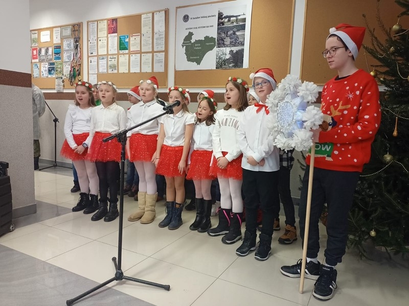 15 uczniów śpiewa kolędy dla żołnierzy. Jeden z uczniów trzyma gwiazdę kolędniczą