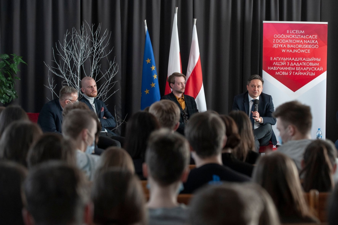 grupa młodzieży podczas spotkania w szkole z Rzecznikiem Praw Obywatelskich; w tle flaga Polski, Unii Europejskiej, Bialorusi oraz banner szkoły