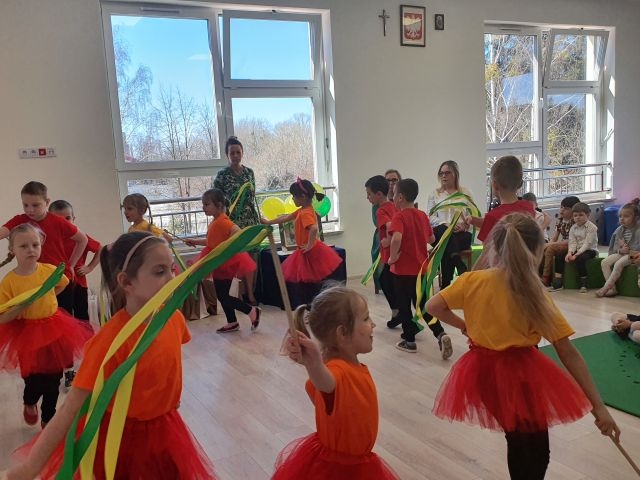 Występ dzieci ubranych w czarno - pomarańczowe stroje.