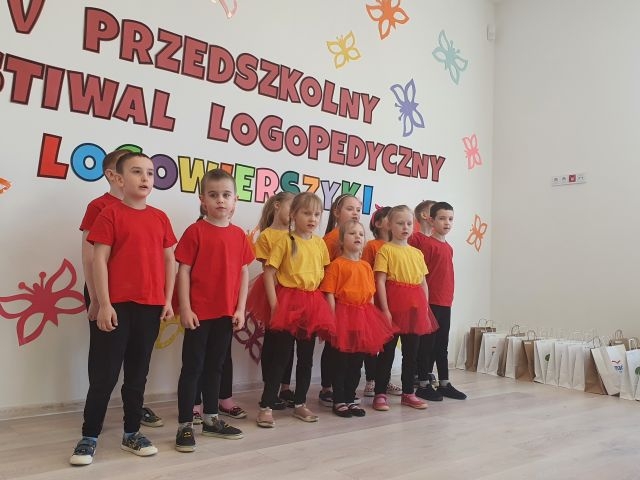 Grupa dzieci ubranych w barwy czarno - pomarańczowe stoi pod ścianą.